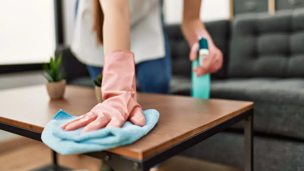 Ett bord torkas av en person med rosa gummihandskar och en blå trasa